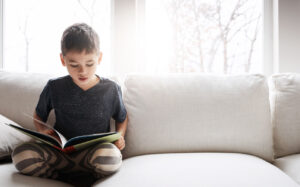 Menino lendo no sofá durante as férias escolares com livros espíritas infantis.