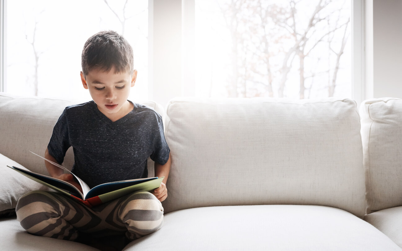 Menino lendo no sofá durante as férias escolares com livros espíritas infantis.